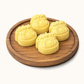 Four yellow flower-shaped mooncakes arranged on a round wooden plate, photographed on a clean off-white background.