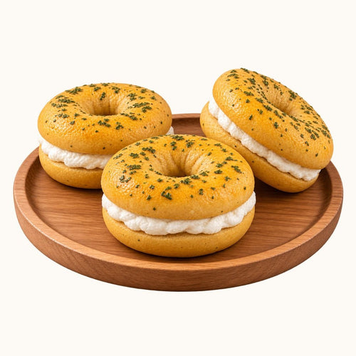 Three bagel halves filled with white cream and topped with green herbs, arranged on a round wooden plate against a plain white background.