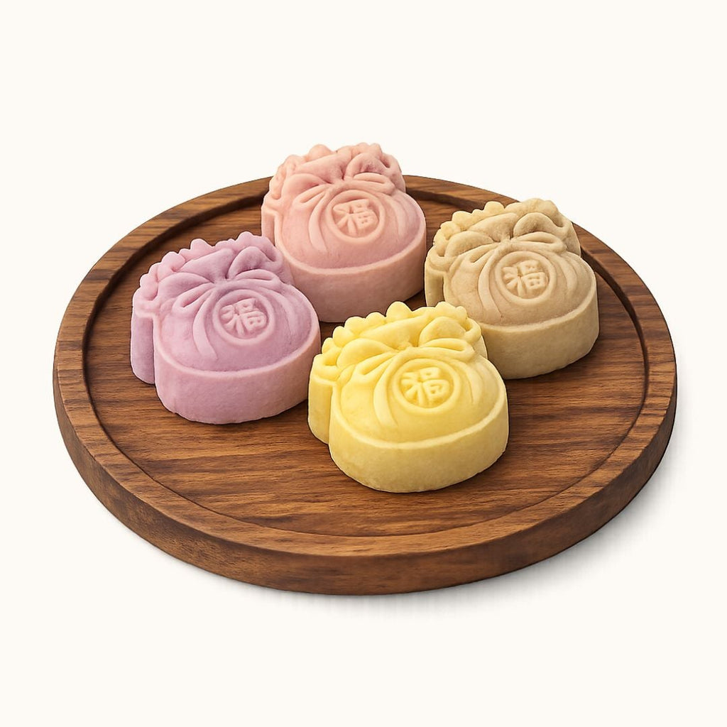 Four decorative mooncakes in pink, yellow, and beige, arranged on a round wooden tray against a clean off-white background.