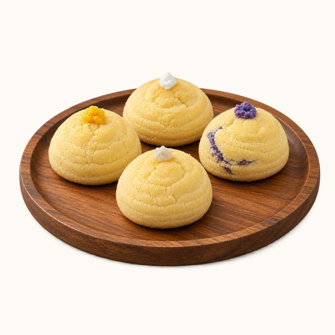 Four small round pastries in pale yellow tones arranged on a round wooden plate against a plain light background.