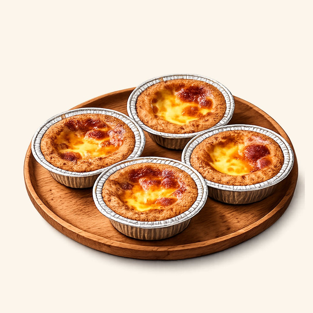 Four mini custard tarts with golden-brown pastry crusts and glossy yellow custard fillings, arranged on a round wooden tray against a light cream background.