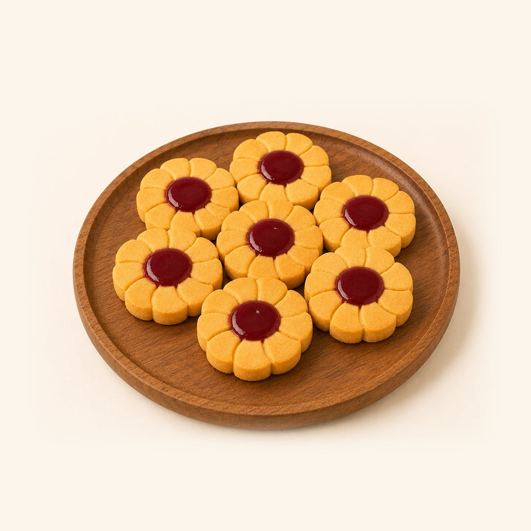 Seven flower-shaped cookies with golden-yellow petals and dark red centers, arranged on a round wooden plate against a solid cream background.